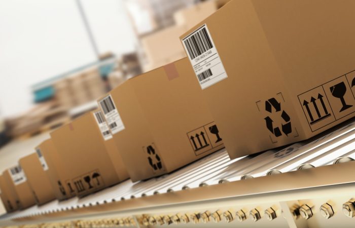 Packed,Courier,On,Production,Line,Against,Cardboard,Boxes,In,Warehouse